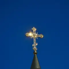 Złoty krzyż prawosławny lśni na tle błękitnego nieba. Symbol nadziei i wiary, często obecny podczas pogrzebu prawosławnego.