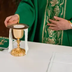 Kapłan w zielonej szacie przygotowuje kielich podczas mszy żałobnej lub pogrzebowej.