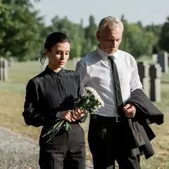 Para pogrzebowa: kobieta w czarnej sukience i mężczyzna w garniturze, trzymający bukiet kwiatów. Wskazówka, jak się ubrać na pogrzeb.