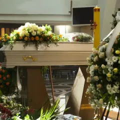 Biała trumna ozdobiona kwiatami, obok pali się wysoka świeca. Czy w niedziele są pogrzeby?