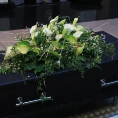 Elegancki wieniec z białych kalii i zieleni spoczywa na czarnej trumnie. To ostatnie pożegnanie, wieniec dla taty.