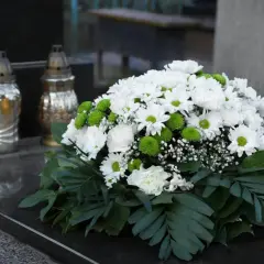 Eleganckie kompozycje na cmentarz: bukiet białych kwiatów z zielonymi akcentami i liśćmi, obok znicze.