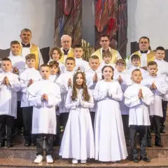 Dzieci w białych strojach komunijnych, z kapłanami, czekają na rozpoczęcie uroczystości. Zastanawiasz się, ile trwa msza?