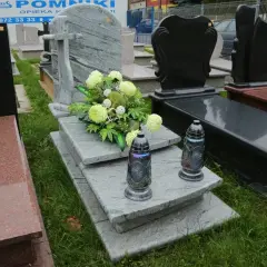 Elegancka dekoracja grobu bez pomnika: szare płyty, bukiet jasnych kwiatów i dwie znicze.
