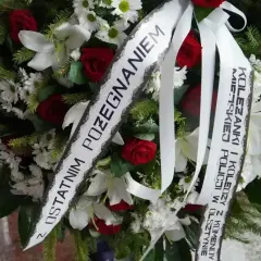Wieniec pogrzebowy z różami i liliami, ozdobiony wstęgami z sentencjami pożegnalnymi.