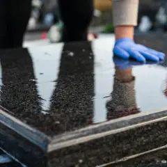 Ręce w niebieskich rękawiczkach polerują mokry granit fioletową ściereczką. Woda i piana świadczą o tym, czym nabłyszczyć granit.
