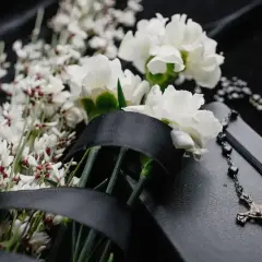 Wiązanka z kalii, ozdobiona czarną wstęgą, leży obok różańca i notatnika.