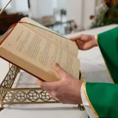 Kapłan w zielonej szacie otwiera księgę podczas mszy pogrzebowej. Teksty liturgiczne pomagają w modlitwie za zmarłego.