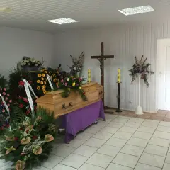 Drewniana trumna otoczona wieńcami i bukietami. Piękne kwiaty na trumnę tworzą smutną, ale pełną szacunku atmosferę.