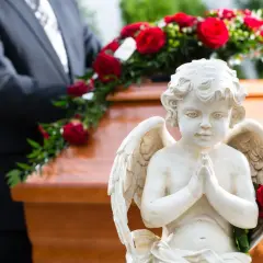 Aniołek czuwa nad trumną, symbolizując spokój duszy po śmierci do pogrzebu. Czerwone róże dodają powagi.