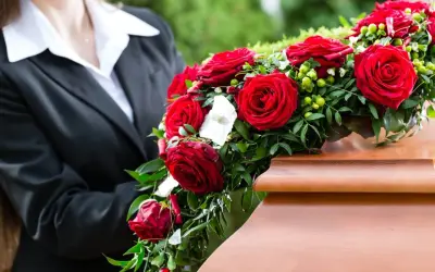 Osoba w czerni kładzie wieniec z czerwonych róż na trumnie. Czy wieniec jest konieczny? To symbol pożegnania.