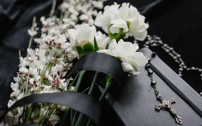 Białe kwiaty, czarna wstęga i różaniec na czarnym tle symbolizują kolory żałoby w Polsce.
