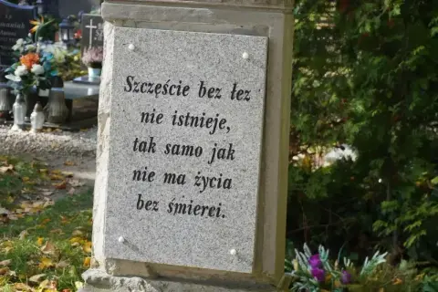 Kamienna płyta z napisem "Szczęście bez łez nie istnieje, tak samo jak nie ma życia bez śmierci". W tle cmentarz, kwiaty i znicze. Prochy po kremacji spoczywają w tym miejscu.