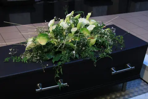 Elegancki wieniec z białych kalii i zieleni spoczywa na czarnej trumnie. To ostatnie pożegnanie, wieniec dla taty.