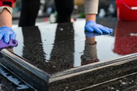 Ręce w niebieskich rękawiczkach polerują mokry granit fioletową ściereczką. Woda i piana świadczą o tym, czym nabłyszczyć granit.