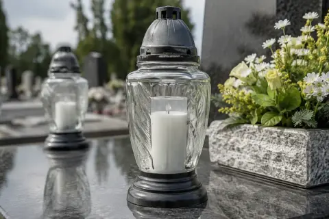 Zapalony znicz na kamiennym nagrobku, symbol pamięci i wiecznego światła. Obok bukiet białych kwiatów.