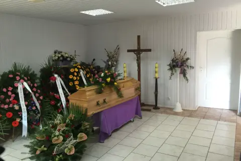 Drewniana trumna otoczona wieńcami i bukietami. Piękne kwiaty na trumnę tworzą smutną, ale pełną szacunku atmosferę.