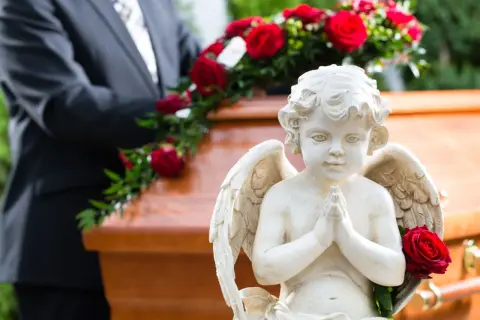Aniołek czuwa nad trumną, symbolizując spokój duszy po śmierci do pogrzebu. Czerwone róże dodają powagi.