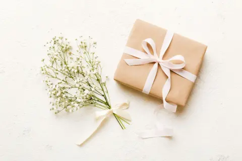 Bukiet gipsówki z kremową wstążką i prezent w papierze kraft, ozdobiony jasnoróżową wstążką. Czy kwiaty daje się w papierze? Tak, w takim eleganckim opakowaniu.