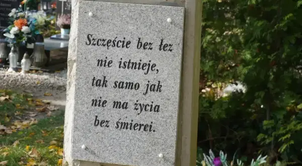 Kamienna płyta z napisem "Szczęście bez łez nie istnieje, tak samo jak nie ma życia bez śmierci". W tle cmentarz, kwiaty i znicze. Prochy po kremacji spoczywają w tym miejscu.