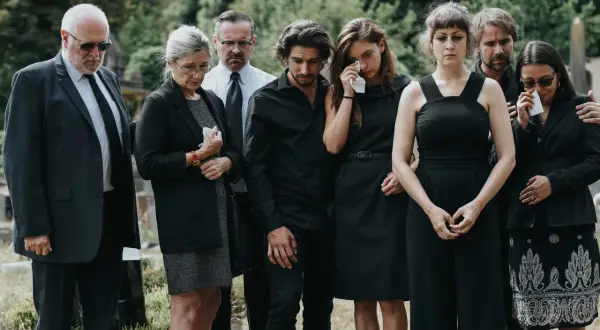 Żałobnicy w czerni, niektórzy płaczą. To smutne wydarzenie, być może pogrzeb świecki, co oznacza brak obrzędów religijnych.