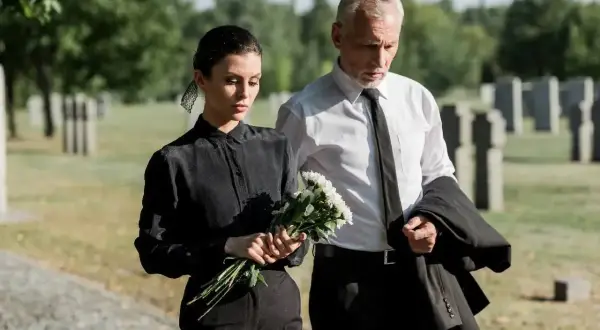 Para pogrzebowa: kobieta w czarnej sukience i mężczyzna w garniturze, trzymający bukiet kwiatów. Wskazówka, jak się ubrać na pogrzeb.