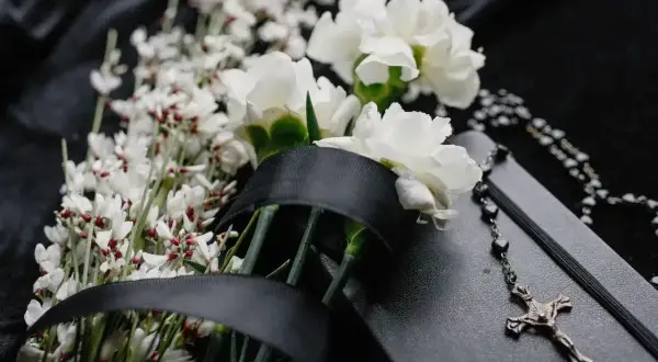 Białe kwiaty, czarna wstęga i różaniec na czarnym tle symbolizują kolory żałoby w Polsce.