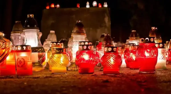 Płonące znicze na cmentarzu. Wiele świec w szklanych pojemnikach, niektóre czerwone, inne żółte, tworzą ciepłe światło. To symbol pamięci i zadumy, często towarzyszy im szczególna pogoda na pogrzebie, co oznacza głęboką refleksję.