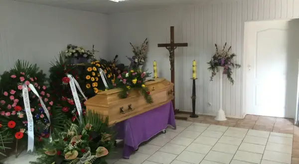 Ostatnie pożegnanie: rzucanie kwiatów na trumnę. Wieniec pogrzebowy i krzyż dodają powagi chwili.