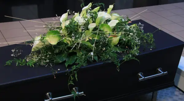 Elegancki wieniec z białych kalii i zieleni spoczywa na czarnej trumnie. To ostatnie pożegnanie, wieniec dla taty.