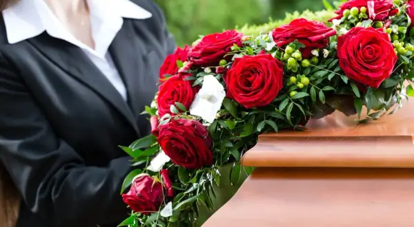 Ostatnie pożegnanie. Wieniec pogrzebowy dla mężczyzny z czerwonych róż i zieleni spoczywa na drewnianej trumnie.