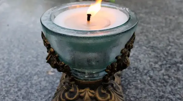 Płonący znicz na kamiennym nagrobku. Dlaczego nie wolno palić zniczy na pogrzebie? To pytanie budzi kontrowersje, ale obraz pokazuje symbol pamięci.