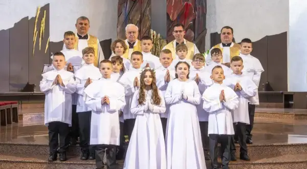 Dzieci w białych strojach komunijnych, z kapłanami, czekają na rozpoczęcie uroczystości. Zastanawiasz się, ile trwa msza?