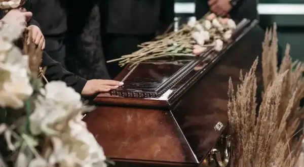 Dłoń na trumnie, kwiaty i suche trawy. Zastanawiasz się, ile trwa różaniec za zmarłego?