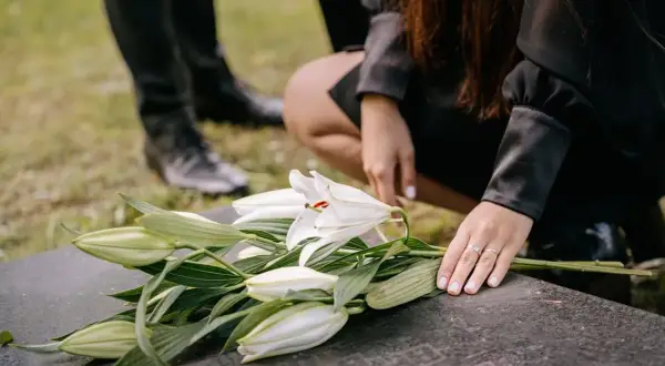 Smutek na cmentarzu. Białe lilie na nagrobku, dłoń z obrączką. Czy przesądy o śmierci w niedzielę mają sens?