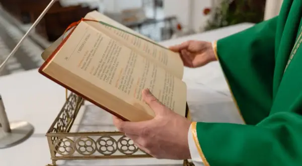Kapłan w zielonej szacie otwiera księgę podczas mszy pogrzebowej. Teksty liturgiczne pomagają w modlitwie za zmarłego.
