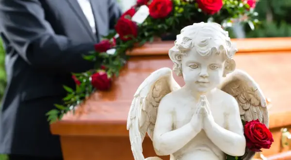 Aniołek czuwa nad trumną, symbolizując spokój duszy po śmierci do pogrzebu. Czerwone róże dodają powagi.