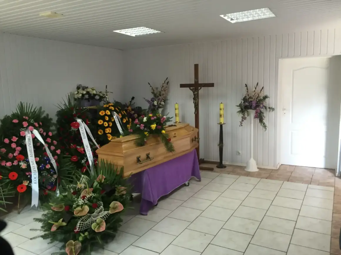 Drewniana trumna otoczona wieńcami i bukietami. Piękne kwiaty na trumnę tworzą smutną, ale pełną szacunku atmosferę.