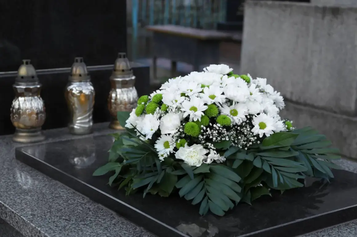 Białe i zielone kwiaty tworzą nowoczesne dekoracje na pomnik. Obok stoją trzy znicze.