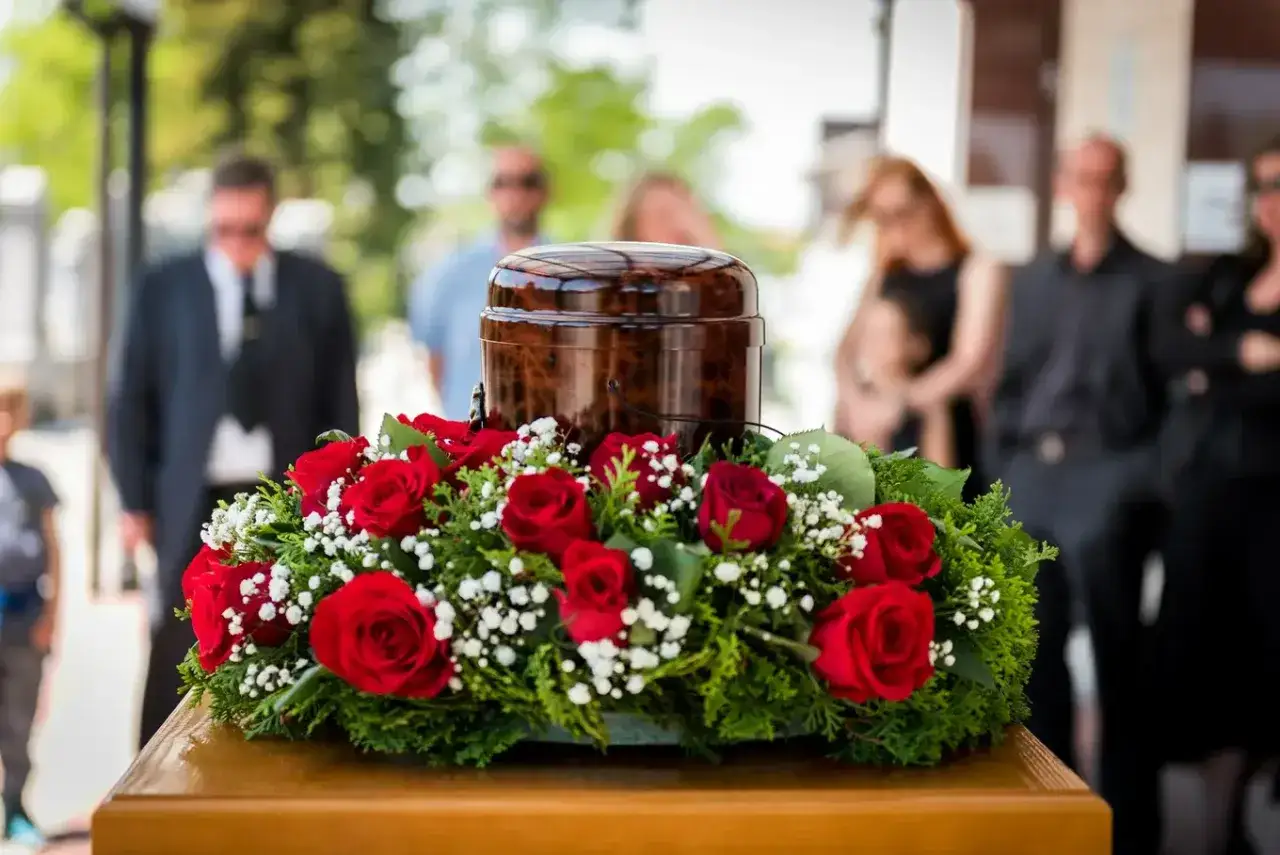 Urzna z czerwonymi różami i zielenią, symbolizująca pożegnanie. W tle ludzie w żałobie. To obraz, który pokazuje, że świecki pogrzeb to pożegnanie bez obrzędów religijnych.