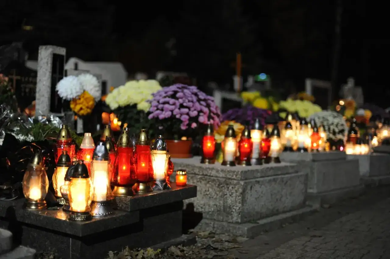 Płonące znicze i kwiaty na grobach, tworząc uroczystą atmosferę na Wszystkich Świętych.