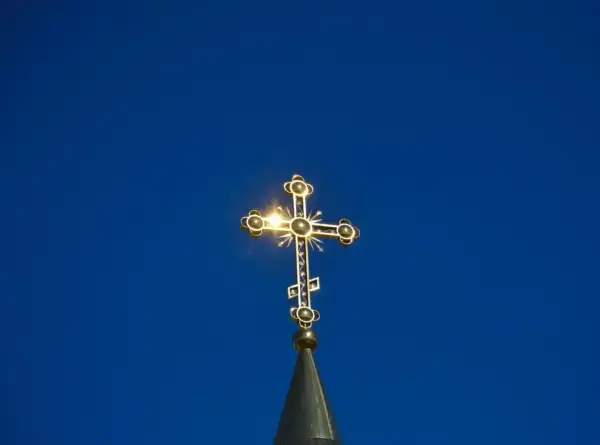 Złoty krzyż prawosławny lśni na tle błękitnego nieba. Symbol nadziei i wiary, często obecny podczas pogrzebu prawosławnego.