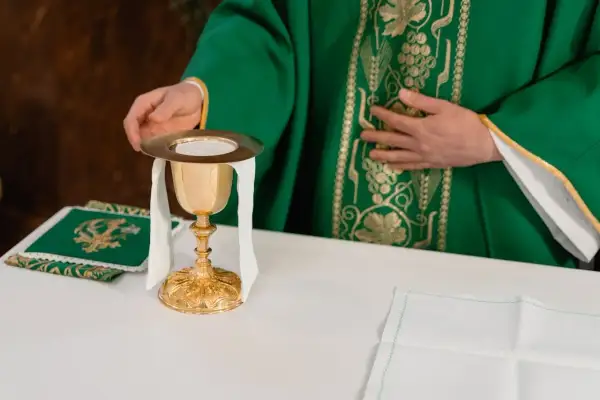 Kapłan w zielonej szacie przygotowuje kielich podczas mszy żałobnej lub pogrzebowej.