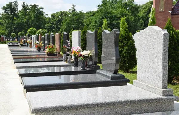 Nowoczesne nagrobki z granitu, co zamiast pomnika na cmentarzu? Rzędy lśniących płyt i geometrycznych form, ozdobione bukietami kwiatów.