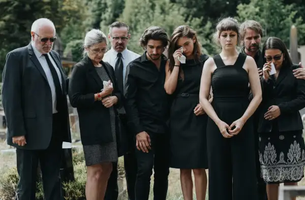 Żałobnicy w czerni, niektórzy płaczą. To smutne wydarzenie, być może pogrzeb świecki, co oznacza brak obrzędów religijnych.