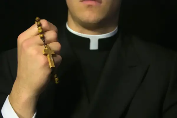 Dłoń księdza trzyma drewniany różaniec. Czy ksiądz może odmówić pochówku? Pytanie o sakramenty.