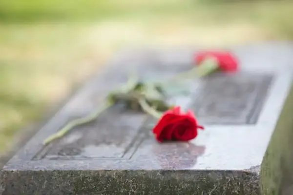 Dwie czerwone róże na kamiennej płycie nagrobnej symbolizują pożegnanie pogrzebowe i wieczną pamięć.