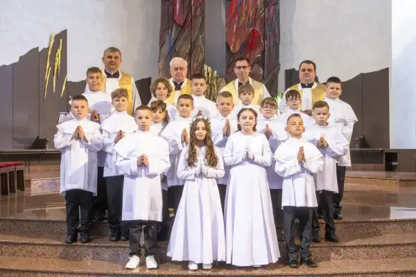 Dzieci w białych strojach komunijnych, z kapłanami, czekają na rozpoczęcie uroczystości. Zastanawiasz się, ile trwa msza?