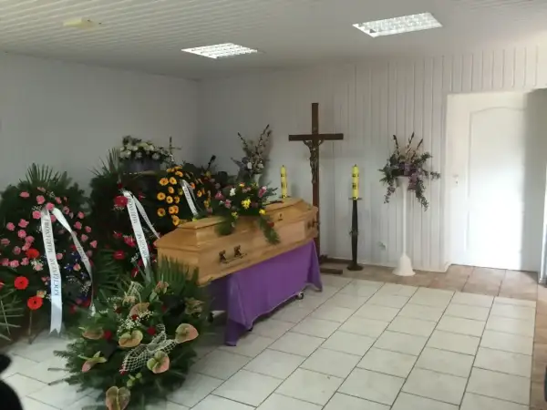 Drewniana trumna otoczona wieńcami i kwiatami, krzyż i świece tworzą najpiękniejsze ostatnie pożegnanie.