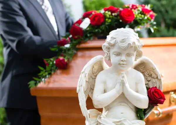 Aniołek czuwa nad trumną, symbolizując spokój duszy po śmierci do pogrzebu. Czerwone róże dodają powagi.